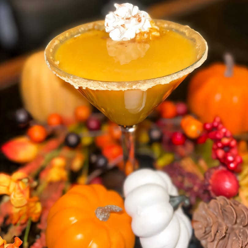 Pumpkin martini with whipped cream and cinnamon, surrounded by autumn decor like pumpkins and berries.